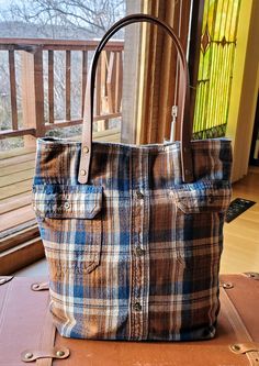 a brown and blue plaid bag sitting on top of a suitcase next to a window