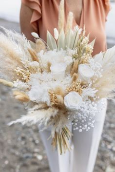 a woman is holding a white vase with flowers and feathers in it on the ground