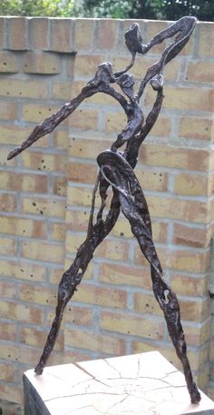 a statue is standing in front of a brick wall and some plants on the ground