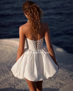 a woman in a short white dress walking on the beach