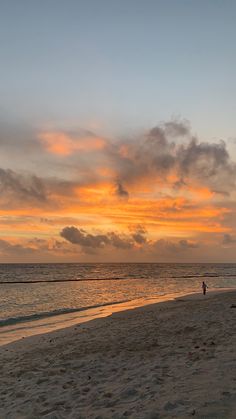 a person walking on the beach with a surfboard under an orange and blue sky