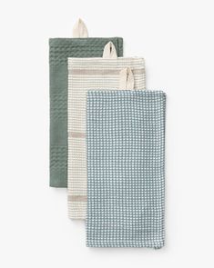 three teal and white kitchen towels on top of each other, one in the shape of a square