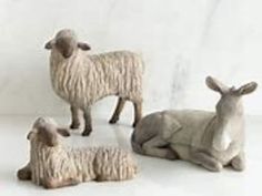 three sheep laying down next to each other on a white surface and one standing up