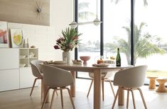 a dining room table with chairs and vases on the table next to large windows