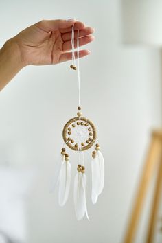 a hand holding a white and gold dream catcher