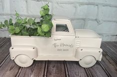 a white truck with a plant in it on top of a wooden table next to a brick wall