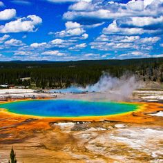 a large blue and yellow crater surrounded by trees on a sunny day with clouds in the sky