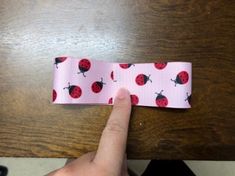 a hand is pointing at a pink ribbon with ladybugs on it and the end has black dots