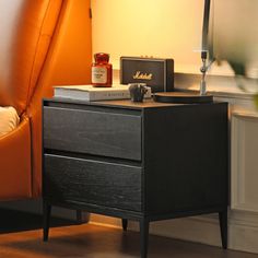 a night stand with a lamp on it next to a bed and orange chair in the background