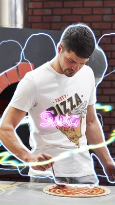 a man standing in front of a pizza on top of a table next to a brick wall