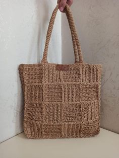 a hand holding a brown knitted bag on top of a white counter next to a wall