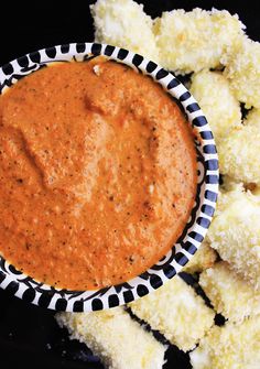 a bowl filled with sauce next to some fried food on a black tablecloth covered plate