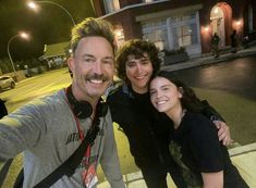 two women and a man taking a selfie in front of a building at night