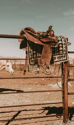 a saddle hanging on a fence with a horse in the background