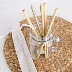 a glass jar filled with wooden sticks on top of a wicker place mat next to a white napkin