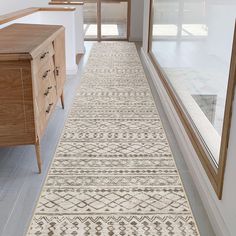 a hallway with a rug on the floor next to a wooden dresser and window sill