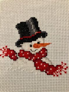 a cross stitch snowman with a red scarf and hat