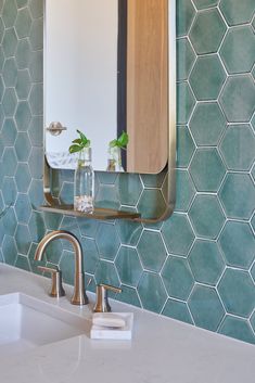 a bathroom sink sitting under a mirror next to a wall mounted faucet in front of a green tiled wall