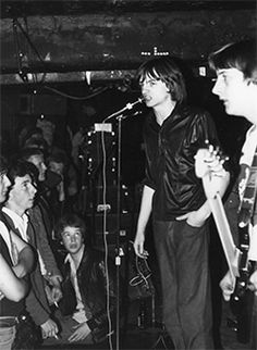 black and white photograph of young men singing into microphones in front of an audience