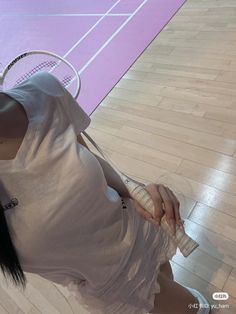 a woman holding a tennis racquet on top of a hard wood floor next to a court