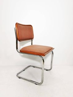 an orange leather chair sitting on top of a metal frame with a white wall in the background