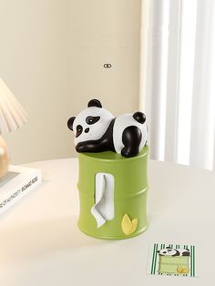 two black and white panda bears sitting on top of a green barrel next to a lamp