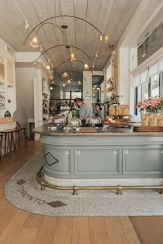 two people are behind the counter in a restaurant with flowers on the table and chairs around it