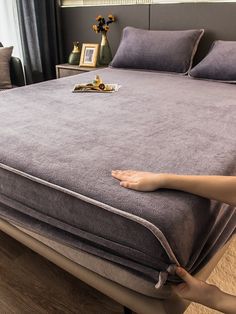 a person reaching for the bottom of a bed that is made up with grey sheets and pillows