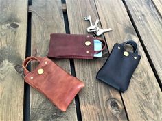 three leather wallets sitting on top of a wooden table next to two keys and a bottle opener