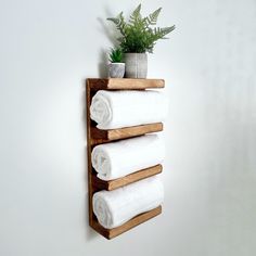 a wooden shelf holding four white towels and a potted plant on top of it