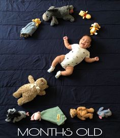 a baby laying on top of a black blanket surrounded by stuffed animals and teddy bears