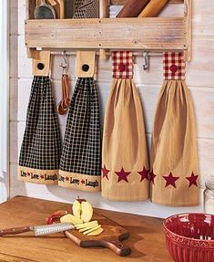 three kitchen towels hanging from hooks on a wooden wall above a cutting board and knife holder