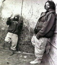 two young men standing next to each other in front of a wall with graffiti on it