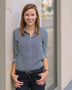 a woman leaning against a wall with her hands on her hips and smiling at the camera