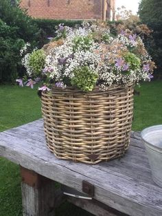 a wicker basket filled with flowers sitting on top of a wooden table in front of a house