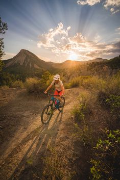 a person riding a bike on a dirt road with the sun setting in the background