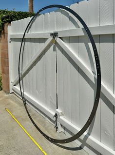 a large metal bike tire on the side of a white fence