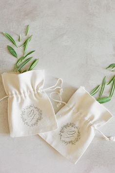 two white linen bags with embroidered designs on them and some green plants in the background