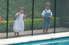 two young children standing in front of a swimming pool with their hands behind the fence