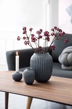 two vases with flowers on a table in front of a grey couch and candle