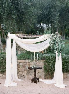 the wedding arch is decorated with white drapes and greenery for an outdoor ceremony