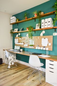 a desk with two white chairs and some plants on the shelves above it, in front of a teal green wall