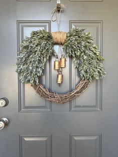 a wreath is hanging on the front door with three golden bells in it and some greenery