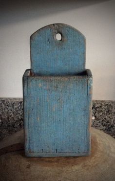 an old blue box sitting on top of a tree stump in front of a white wall