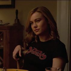 a woman sitting at a table with a glass in front of her and another person standing behind her