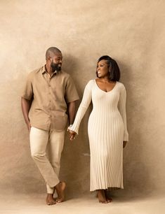 a man and woman standing next to each other in front of a beige wall holding hands