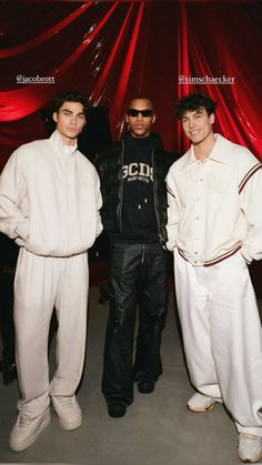 three young men standing next to each other in front of a red curtain and wearing white pants