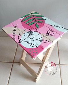 a small wooden stool painted with flowers and leaves on the top, sitting on a tile floor