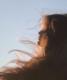 a woman with long hair blowing in the wind on a sunny day, looking into the distance