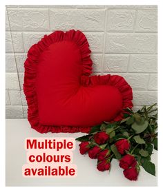 a red heart shaped pillow sitting on top of a white table next to some roses